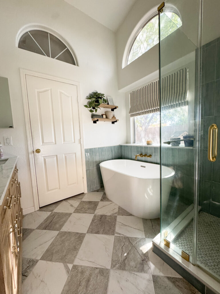 Bright modern bathroom with affordable porcelain checkerboard tiles, freestanding soaking tub, brass fixtures, blue-green subway tile walls, and arched windows above shower